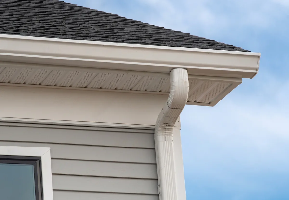 White aluminum gutter and downspout on a corner of a house with new soffit and fascia under gray asphalt shingles