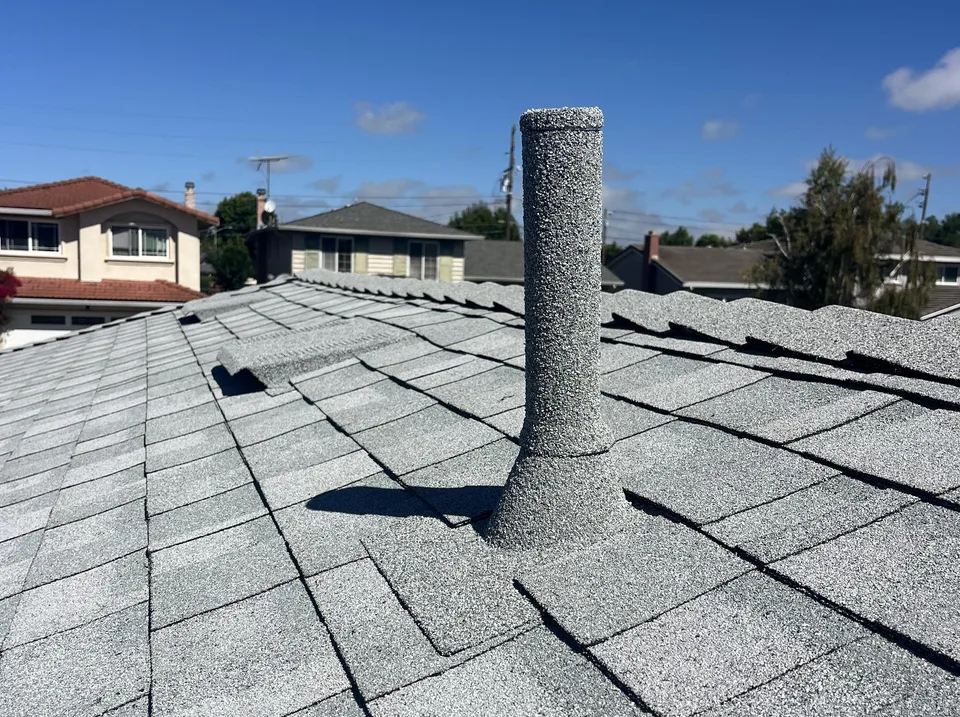 Plumbing vent pipe sleeved in gray stone coating matched to the shingle color, on a stone-coated flashing base tucked into the shingle courses of a Sonrise roof